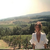 a woman in a white dress standing in front of a vineyard