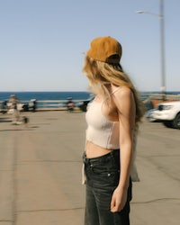 a woman wearing a hat and jeans standing on a pier