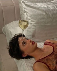 a woman laying in bed with a glass of wine on her head