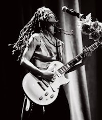 a black and white photo of a woman with dreadlocks playing a guitar