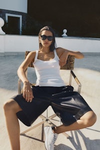 a woman sitting on a chair wearing a white tank top and black shorts